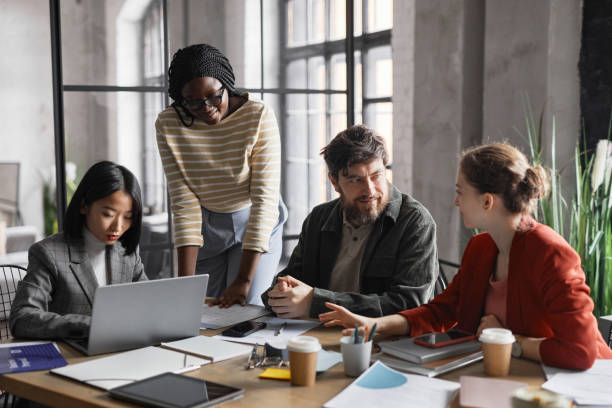 Multi-ethnic group of business people discussing project while sitting at meeting table in graphic office interior