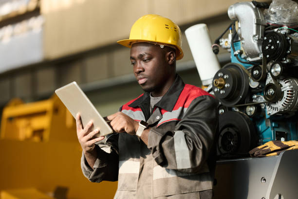 Serious young foreman or control manager in safety helmet and workwear scrolling through online technical information in tablet