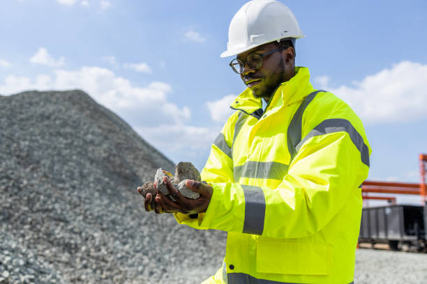 Railroad worker holding building rocks ballasts for road construction.Worker in protective helmet and jacket holding rock used for road and railroad construction.